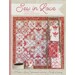 Front of Sew In Love, a wall hanging replete with pinks, whites, creams, and red, with a ladder to the right side holding three other quilted projects