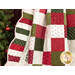 Close up photo of a green, red, and cream Christmas-themed quilt draped with a decorated Christmas tree beside it