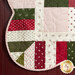 Close up photo of one corner of a green, red, and cream Christmas-themed quilt hanging on a red paneled wall 