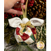 Close up photo of a finished Angel Bell Ornament being hung on a branch of a decorated Christmas tree with pinecones and glittering berries in the background