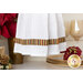 Close up photo of the bottom of a hanging towel made with metallic striped Christmas fabrics hanging on front of a white shelf containing a poinsettia, gold dishware and winter decor items