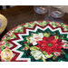 Close up of the table topper showing detail in prairie points and floral fabrics on a wooden table with glasses and a plate in the background