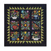 Photo of the finished Folk Art Sampler quilt featuring colorful stylized floral motifs on a black background, isolated on a white background