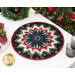 Photo of a round table topper decorated with prairie points and made with Christmas fabric resting on a white table top with gray glasses and Christmas decor including a decorated Christmas tree in the background.