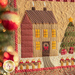 A green paneled wall with a small wall hanging depicting a house in a snowy field with a Christmas tree in the yard decorated with wrapped gifts. Christmas decor is all around the wall hanging with a decorated tree in the foreground.