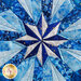 Close up photo of the center of the completed quilt block featuring a pinwheel shaped snowflake made with different shades of blue fabric.