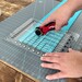 person using rotary cutter and quilting ruler on a grey cutting mat