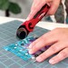 person using a red and black rotary cutter with quilting ruler and cutting mat