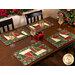 Photo of four place settings with Magic Stained Glass Placemats and wine glasses with a wrapped gift on the table and Christmas decor, and poinsettias in the background
