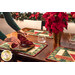 Photo of a cloth napkin being added to a place setting with four Magic Stained Glass Placemats, Christmas decor, and poinsettias.