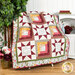 Photo of a red, cream, pale blue, and golden yellow quilt made with traditional quilt star piecing designs and rectangular blocks with quotes from psalms interspersed, draped over furniture with houseplants, red flowers, and decor on either side.