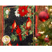 Photo of a winter themed panel quilt featuring a panel with red cardinals and poinsettias on a black background with a rustic textured border, hanging flat on a wall with a decorated Christmas tree in the foreground.