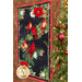 Photo of a winter themed panel quilt featuring a panel with red cardinals and poinsettias on a black background with a rustic textured border, hanging flat on a wall with a decorated Christmas tree in the foreground.