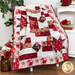 Photo of the finished quilt draped over a chair with red floral decor, books, white furniture, and plants in the background.