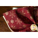 Close up photo of a red cloth napkin in a napkin ring on a wooden table, showing fabric details of metallic snowflakes