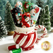 Colorful fabric rolls in a festive striped mug, surrounded by miniature Christmas trees.