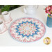 The completed French Roses Point of View Kaleidoscope Folded Star Table Topper staged on a table with a teapot and mugs 