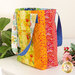 Photo of a large jelly roll tote bag sitting on a small white table with a houseplant and bouquet in the background.
