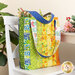 Photo of a large jelly roll tote bag sitting on a small white chair with a houseplant, small white table, and bouquet in the background.