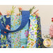 Close up photo of a large jelly roll tote made with bright floral fabrics filled with flowers with a white table and bouquet in the background.