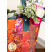 Close up photo of a large jelly roll tote made with orange abstract fabric filled with a floral bouquet with a white table and house plant in the background