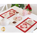The two completed Tea & Cookies for Two - February placemats, staged on a white table with red roses, white teacups with tea, a round white teapot, a pearlescent pink teapot, and frosted heart shaped cookies with pink and red sprinkles. A small indoor plant can be seen behind the table. 