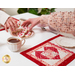Two people enjoying tea and cookies with the placemats; just their arms are visible, both reaching for a cookie.