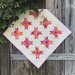 A photo of a completed variation of the quilt draped over a rustic grey fence outside