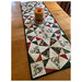 The completed Just a Sliver tablerunner, staged on a wood table with a candle in the center