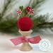 The pins in action on a red wool ball, staged atop a wooden spool and with a pine bough in the background.