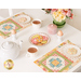 The two completed April placemats facing each other, staged atop a white table. Plates with decorated cookies sit atop each placemat beside white tea cups, a pink sugar jar, egg cups, and a green pot of spring flowers.