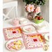 The two completed June placemats, colored in bright pink, red, white, and yellow, staged on a white table with coordinating decor. On white scalloped plates sit beautifully frosted flower and butterfly cookies.