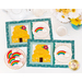 A top down shot of the two completed Tea & Cookies placemats for August, colored in bright yellow, teal, and cream, staged on a white table with white teacups and coordinating cookies.