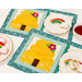 A top down shot of the two completed Tea & Cookies placemats for August, colored in bright yellow, teal, and cream, staged on a white table with white teacups and coordinating cookies peeking out from the left and right sides of the frame.