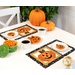 A plate of frosted jack-o-lantern cookies and two full cups of tea sit in the middle of a staged table with two completed October mats in orange, black, and white.