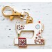 The sewing machine enamel charm out of its packaging, staged on a textured white wood background.