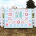 The completed quilt, staged over a white fence on a bluesky day.