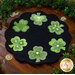 The completed wool mat, staged on a rustic cherry wood table, surrounded by a green garland and tossed golden coins.