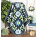 The Edelweiss quilt, completed in navy blue, powder blue, green, and white, draped over a ladder and staged beside coordinating plants, furniture, and decor.