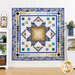 The completed Medallion quilt in blue, teal, and gold from the Jaikumari collection. Staged on a white paneled wall, the quilt is bordered by white furniture holding color-coordinated housewares such as flowers, a lantern, books, and plants.