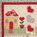 A close up on one of the blocks, showing fabric and stitching detail on a red-roof cottage with hearts and a heart plant.