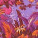 close up of Rich light purple fabric with sprawling foliage and florals in orange, burnt sienna, magenta, and pink, with black shadows and cream highlights.