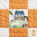 A pieced fabric block featuring white and orange fabric with a small scene of a bunny, cottage, and roses in the center