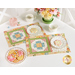 The two completed April placemats, colored in cheerful spring colors, staged atop a white table. Plates with decorated cookies sit atop each placemat beside white tea cups, a pink sugar jar, and a green pot of spring flowers.