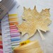 The featured project, a highly detailed leaf, staged beside the swatch book and a large spool of thread.