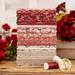 A photo of a stack of fabrics in Rouenneries Trois FQ Set in red, pink, gray, and cream set next to roses and thread spools