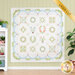 The completed Hope Blooms quilt in white, cream, blue, pink, and green, hung on a green paneled wall and staged with a house plant and white shelf that holds coordinating wares. A yellow banner reads 