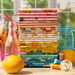 A photo of colorful, modern fabric in a stack against a window set next to colorful jars, thread, and lemons
