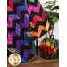 A shot of the draped quilt, demonstrating contrast between the black and vibrant rainbow colored fabrics. A basket of rainbow florals sits beside the quilt.