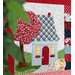 A close up on a block with a light blue house and red tree. From the left side of the photo, a houseplant peeks into frame.